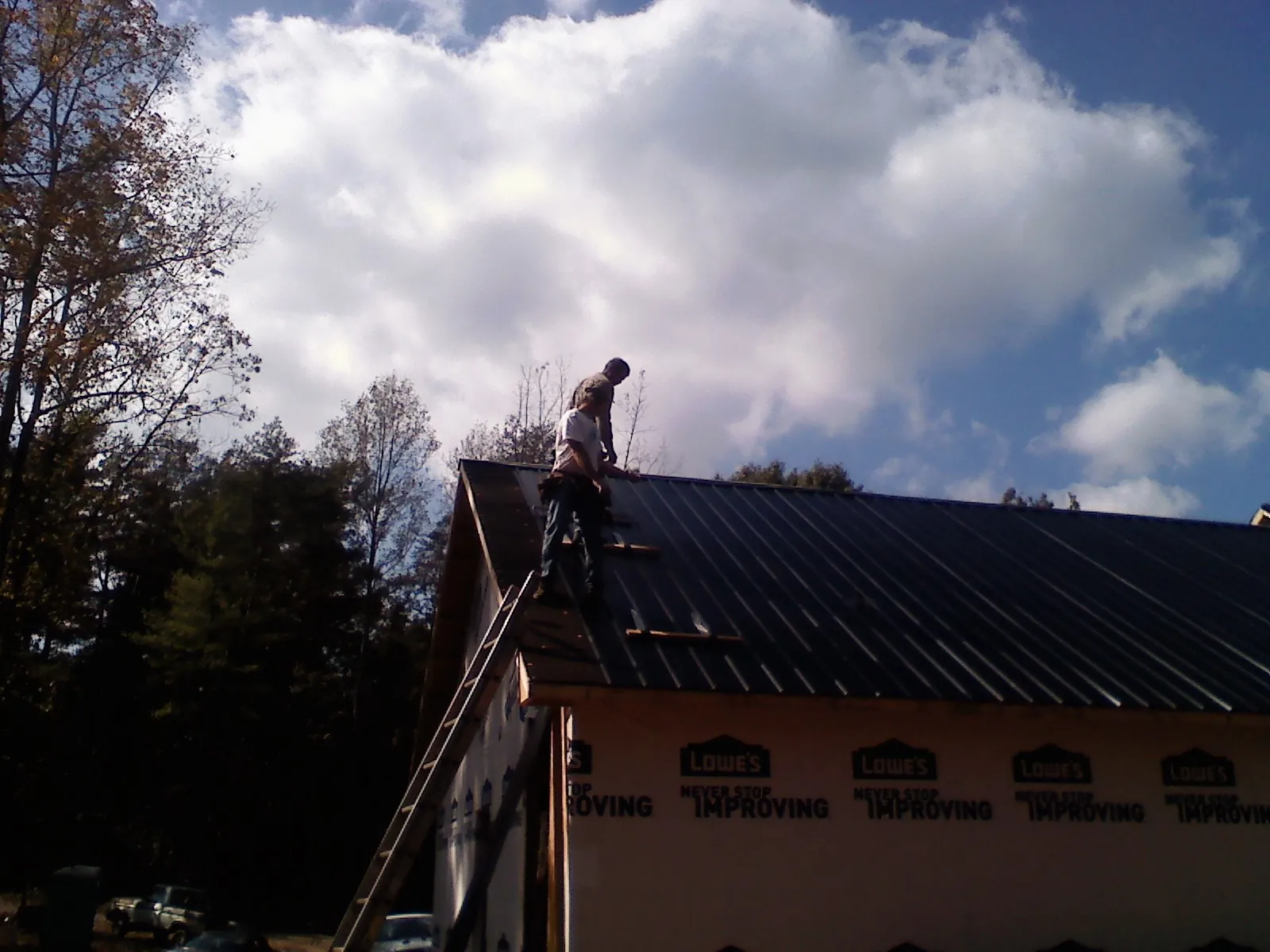 Roofer fastening dark metal panels high against a cloudy sky, from a Roof Inspection job in Rockbridge