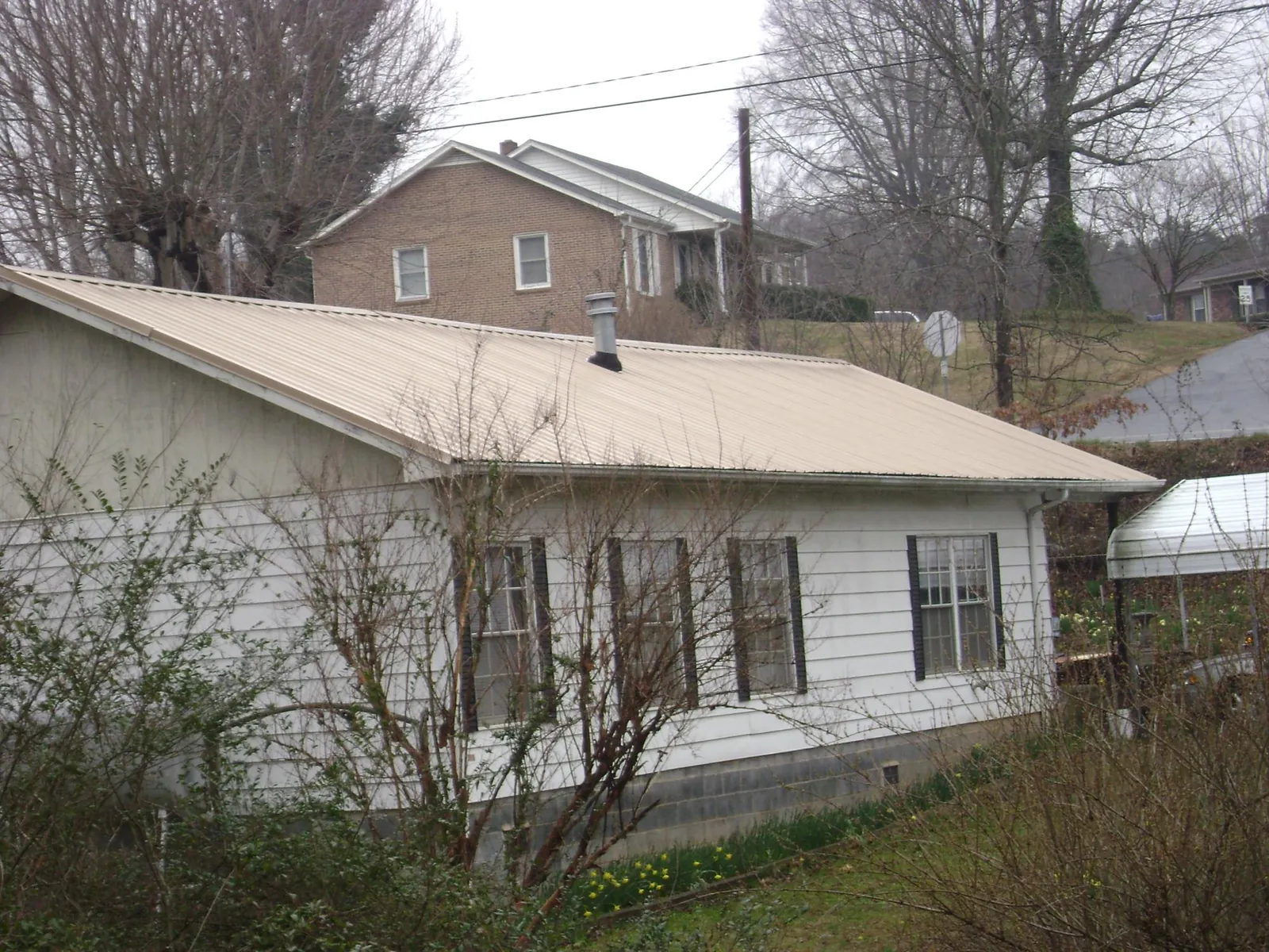 Tan metal roof on a white sided house set into a hillside — Commercial Roofing by Roofing Brothers in Rockbridge